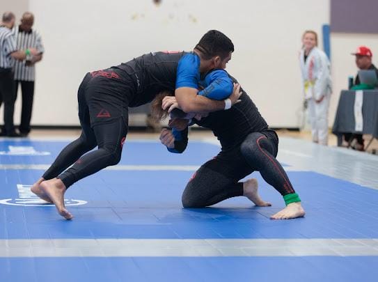 Two athletes grapple on a blue mat during an intense brazilian jiu-jitsu competition.